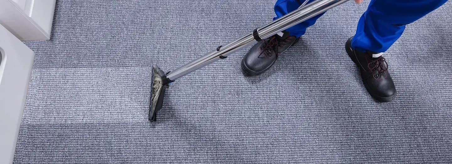 Carpet cleaner in blue workwear cleaning a grey carpet with an extraction wand